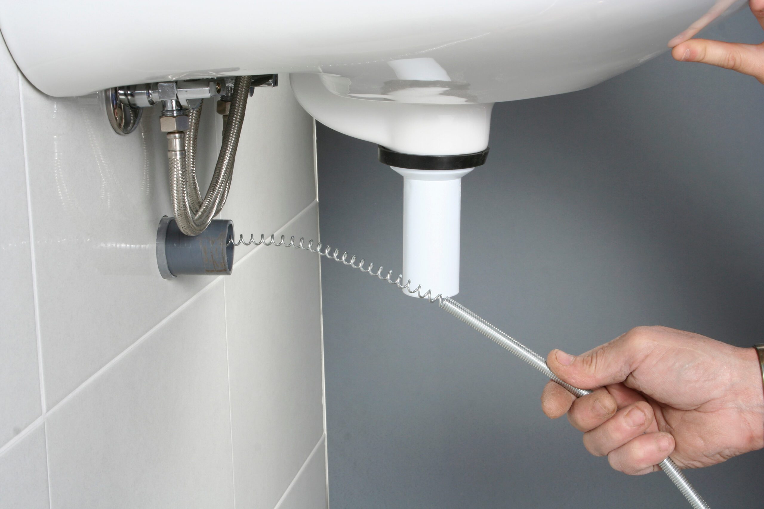 A person uses a plumbing snake to clear a clog in a pipe under a sink., Plumber in Bellview - FL tightening a supply connection beneath a bathroom vanity during repair